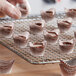 A hand holding a tray of chocolates with brown Novacart boat baking cups.