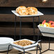 A white Libbey square porcelain plate with food on a table in a hotel buffet.