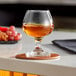 A Libbey brandy glass filled with brown liquid on a coaster.