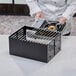 A person holding a black rectangular metal Chef Master Butane stove cover with metal grates.