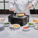 A chef cooking food on a Chef Master collapsible butane stove with a black cover.