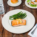 A Libbey Farmhouse cream porcelain plate with a piece of salmon, green vegetables, and lemon wedges on top.