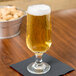 A Libbey stemmed pilsner glass of beer on a napkin next to a bucket of peanuts.