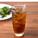A Libbey cooler glass of iced tea with a straw next to a plate of salad.