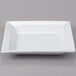 A white square porcelain soup bowl on a white square plate.