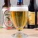A Libbey Banquet goblet filled with beer next to a bottle of beer.