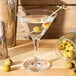 A Libbey Embassy martini glass with a martini and olives on a table.