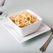 A Libbey white porcelain bouillon bowl filled with soup on a plate with a spoon.