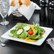 A Libbey Ultra Bright White wide rim square porcelain plate with salad and bread on a table.