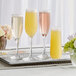 A white tray with three Libbey Embassy champagne flute glasses filled with yellow liquid and flowers.