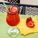 A Libbey Poco Grande glass of red liquid with ice, strawberries, and a straw on a napkin.