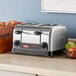 A Hatco commercial toaster on a kitchen counter with a metal basket of green and red apples on top.