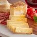 A cutting board with Sartori Tomato Basil BellaVitano cheese, bread, and tomatoes.