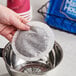A hand holding a round white coffee filter over a cup.