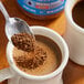 A spoon scooping brown Maxwell House Original Roast Instant Coffee granules.