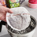 A hand holding a round white paper with red text over a metal coffee filter basket.