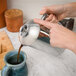 A person using a Frieling stainless steel French press to pour coffee into a cup.