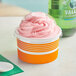 A close up of a Choice orange paper frozen yogurt cup filled with pink frozen yogurt.