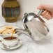 A hand pouring tea into a Primo stainless steel teapot.