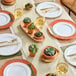 A table with Visions white plastic bowls with gold beaded rims, plates, and utensils.