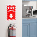 A red and white "Fire Extinguisher" safety label with down arrow next to a fire extinguisher on a wall.