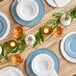 A table set with white plates with silver beaded rims and glasses on a table at a catering event.