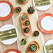 A table setting with white Visions plastic bowls with gold beaded rims, plates, and silver utensils.