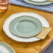 A Visions Eucalyptus plastic plate with gold trim on a table set with wine glasses.