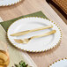 A table setting with a Visions white plastic plate with a gold beaded rim, fork, and knife.