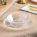 A clear plastic bowl with a gold beaded rim on a table set with clear plastic bowls and plates.