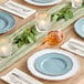 A table setting with Visions Steel Blue plastic plates, glasses, and candles.