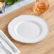 A Visions white plastic plate with a silver vintage rim on a table with a knife and silverware.