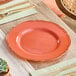 A Visions Terra Cotta plastic plate with a gold vintage rim on a table with other plates and utensils.