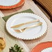 A Visions white plastic plate with a gold beaded rim, a fork and knife on it.