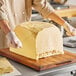 A person cutting a large block of Cabot Grade AA unsalted butter on a counter.