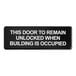 A black sign with white text that says "This door to remain unlocked when building is occupied"