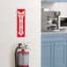 A red and white Lavex fire extinguisher safety label with down arrow on a wall above a fire extinguisher.