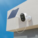 A white Reolink Argus series camera mounted on a wall with a solar panel attached.