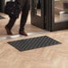 A person walking past a black rectangular Lavex entrance mat on a wood floor.