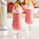 Two glasses of pink strawberry milkshakes with whipped cream and strawberries on top.