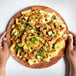 A person's hand holding a plate of nachos with Barvecue Plant-Based Vegan Carnitas, black beans, and avocado.