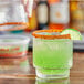 A glass with a green drink rimmed with Twang Chile Lime Rimming Salt and a lime wedge.