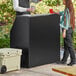 A man and woman standing next to a Lancaster Table and Seating Foldaway Bar on a table in an outdoor catering setup.