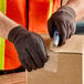 A person wearing Lavex brown jersey gloves using a box cutter to cut a box.
