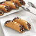A plate with Vaccaro's mini cannoli shells on it with a fork.