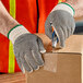 A person in Lavex work gloves using a cutter to cut a cardboard box.