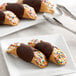 A white plate with two Vaccaro's Mini Chocolate Cannoli shells topped with sprinkles and chocolate.