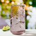 A close up of an Anchor Hocking Brockhill rosewater pink cooler glass filled with water, ice, and a lime wedge.