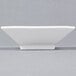 A CAC Citysquare white square porcelain bowl on a gray surface.