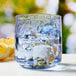 A close up of an Anchor Hocking Coastal Blue Rocks glass filled with water, ice, and a lemon.